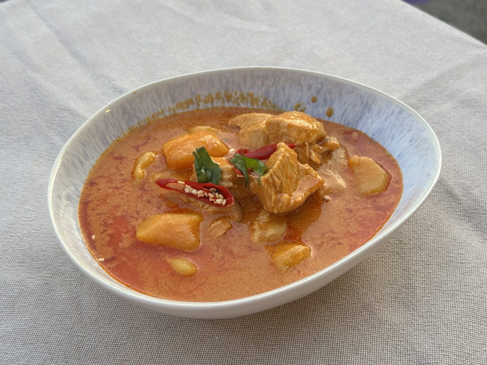 Cremiges rotes Curry mit Hühnchen und Kartoffeln in einer blauweißen Schale